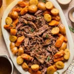 instant pot chuck roast shredded on a platter with carrots and potatoes around it.