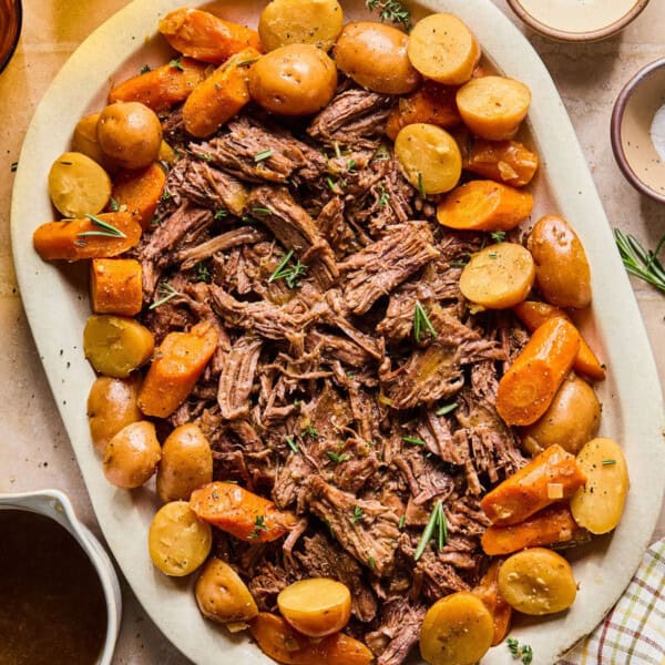 instant pot chuck roast shredded on a platter with carrots and potatoes around it.