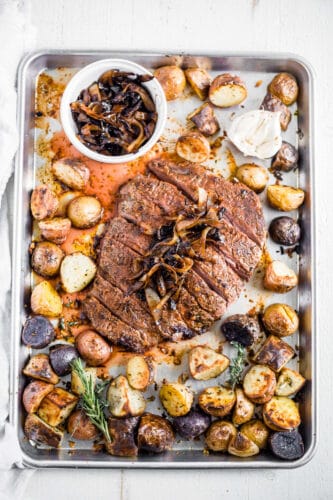 flank steak recipe on sheet pan with herbs, garlic, potatoes and caramelized onion