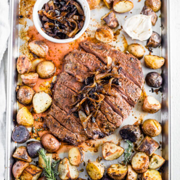 flank steak recipe on sheet pan with herbs, garlic, potatoes and caramelized onion