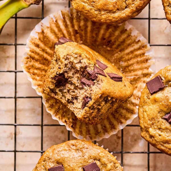 Golden almond flour banana muffins unwrapped on a cooling rack with a bite taken out, showing soft texture.