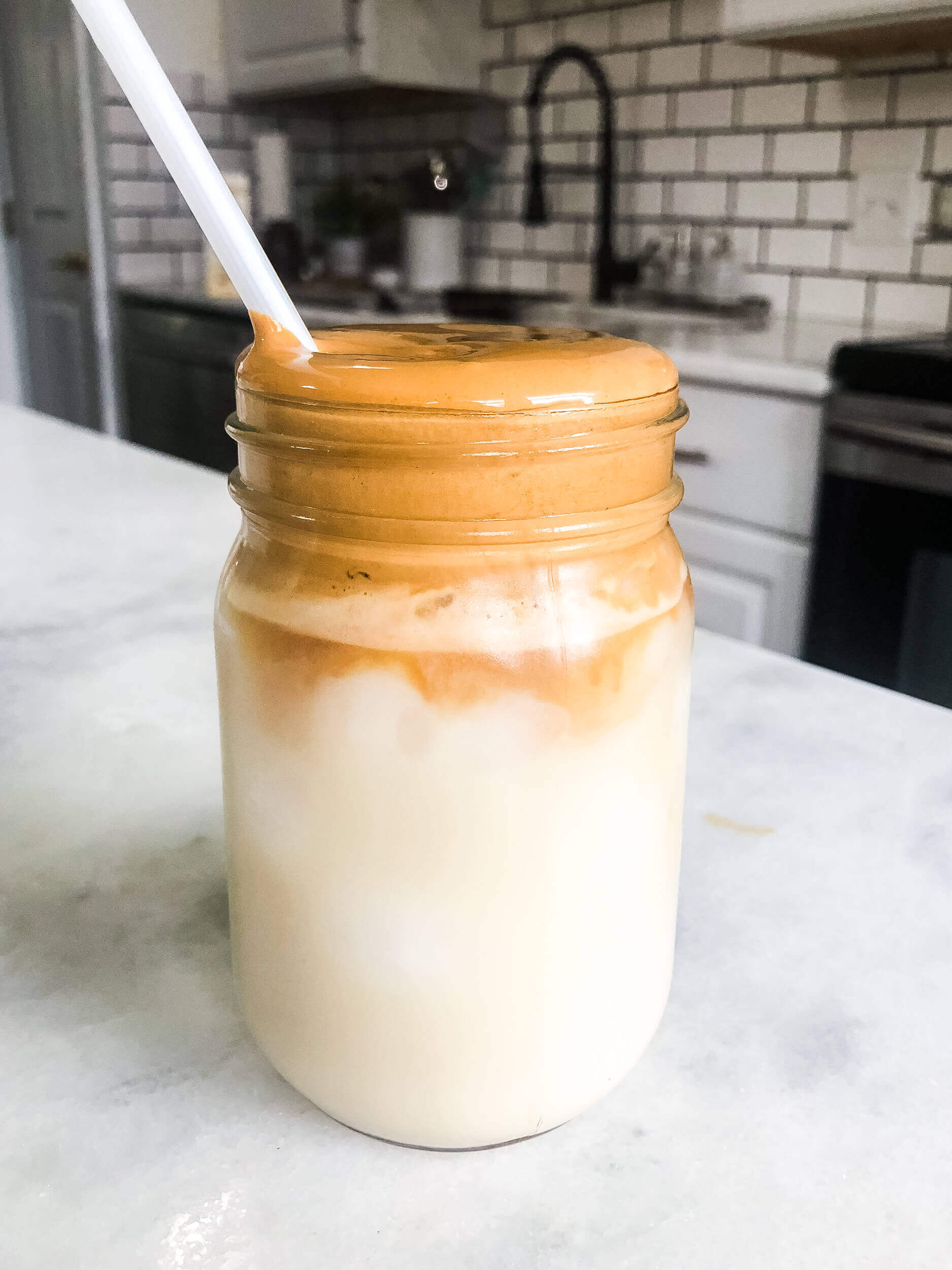 dalgona whipped coffee on top of ice cold oat milk in a mason jar