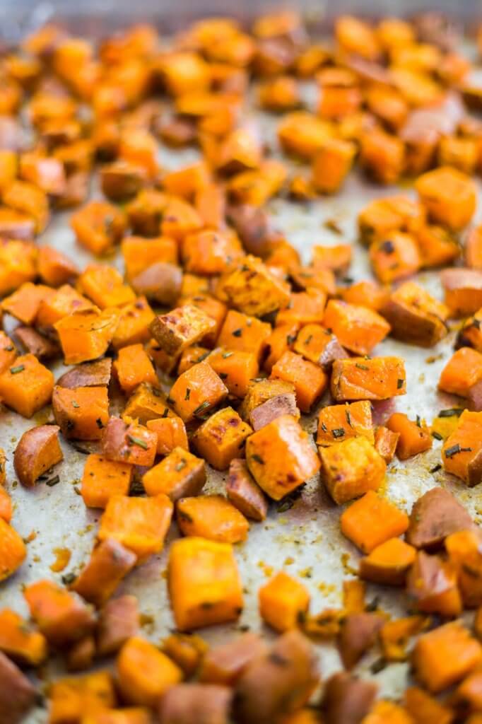 cubed sweet potatoes roasted with olive oil and fresh rosemary on a sheet pan