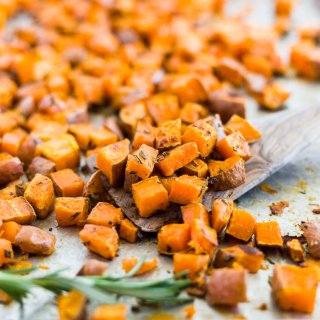 cubed and roasted sweet potatoes on a sheet pan with a wooden spoon and fresh rosemary