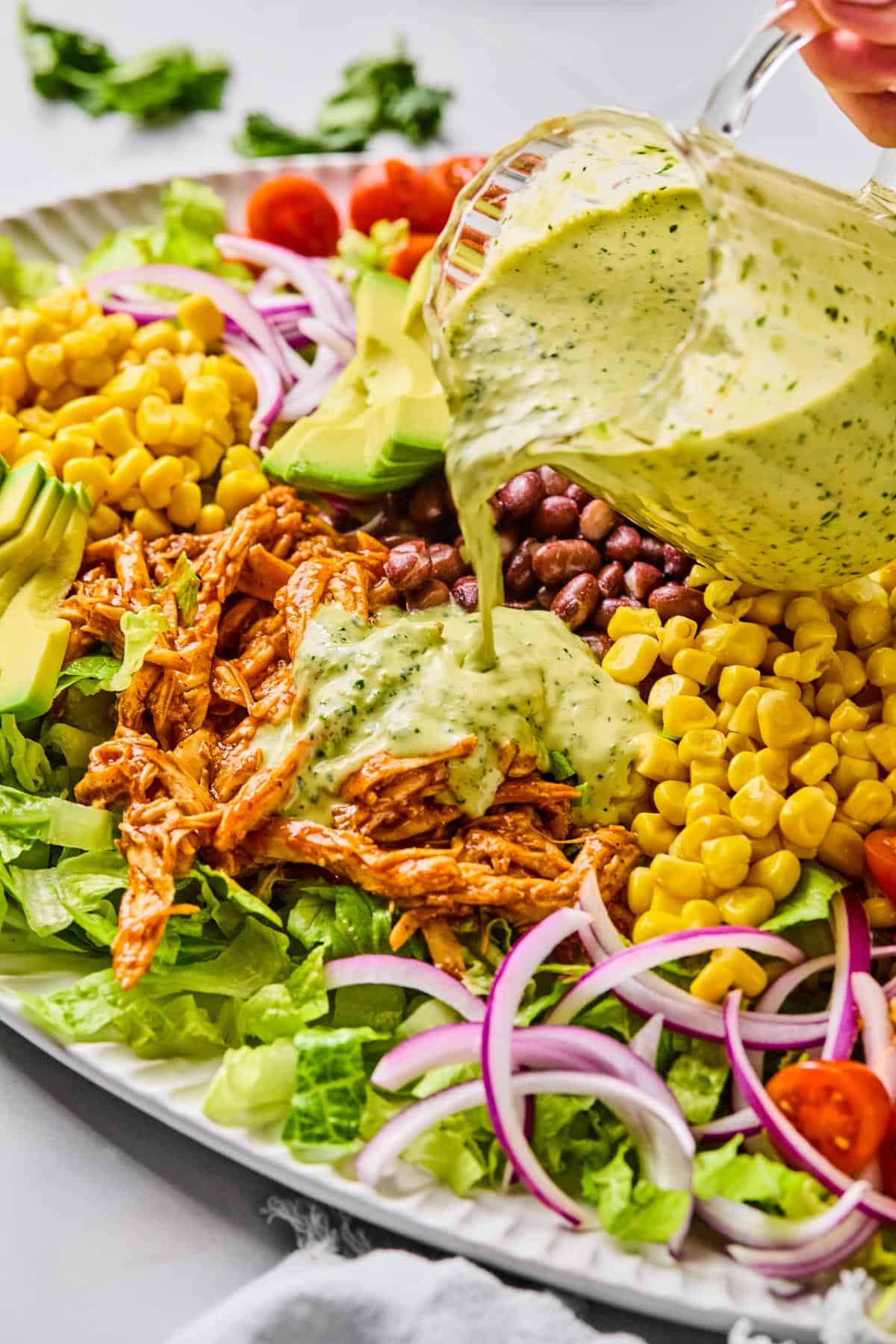 creamy jalapeno dressing being poured onto bbq chicken salad