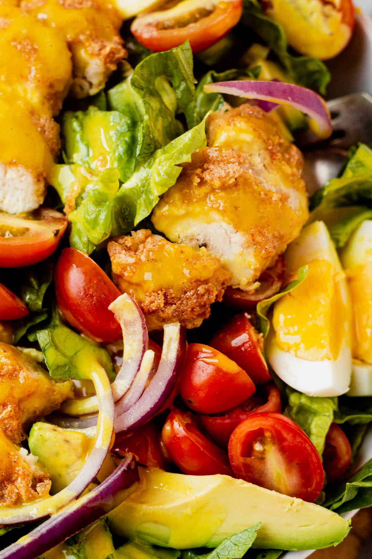 crispy chicken strips on top of a salad covered in honey mustard