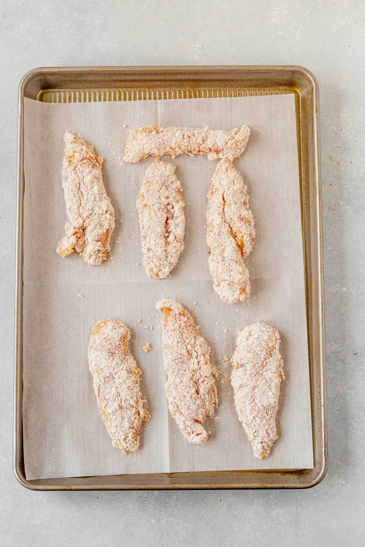 chicken tenders dredged in flour on a baking sheet