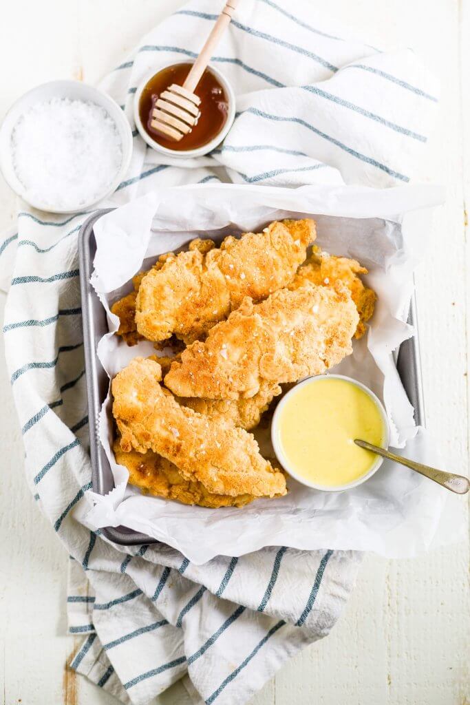 paleo fried chicken tenders on parchment paper with a bowl of honey mustard