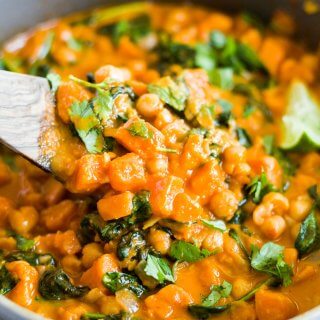 wooden spoon scooping out sweet potato coconut curry from the pot
