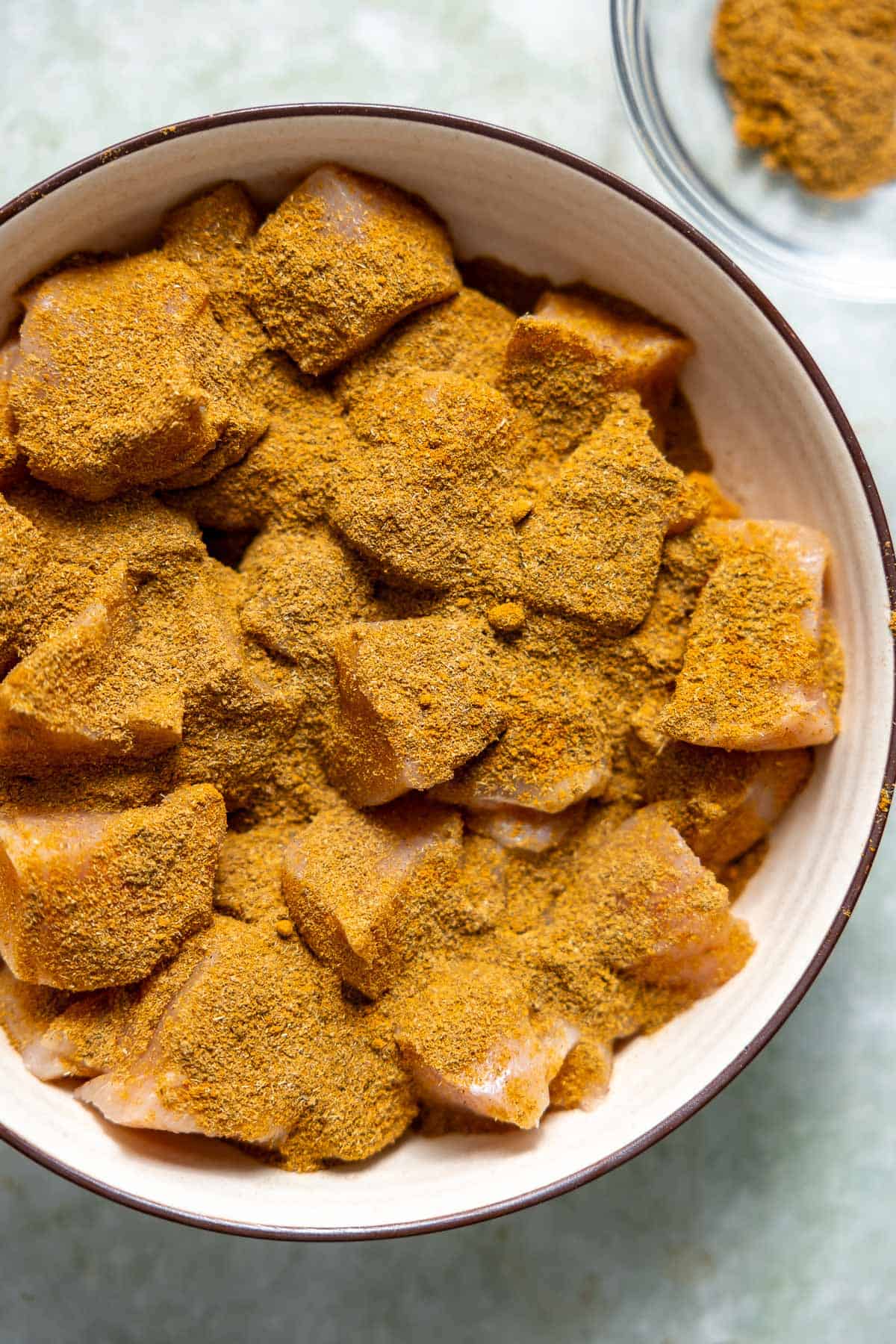 diced chicken breasts seasoned with curry powder and coriander in a mixing bowl.