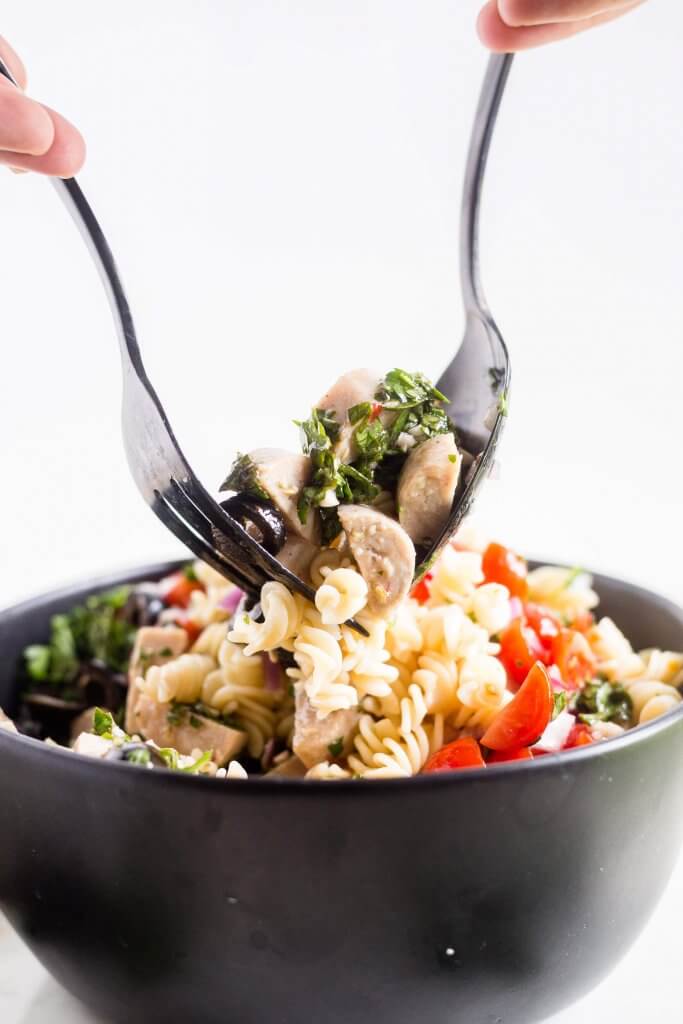 large black fork and spoon mixing Italian pasta salad in a black bowl