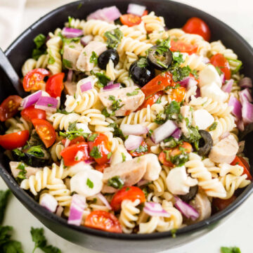 Italian pasta salad in a black bowl with fresh herbs