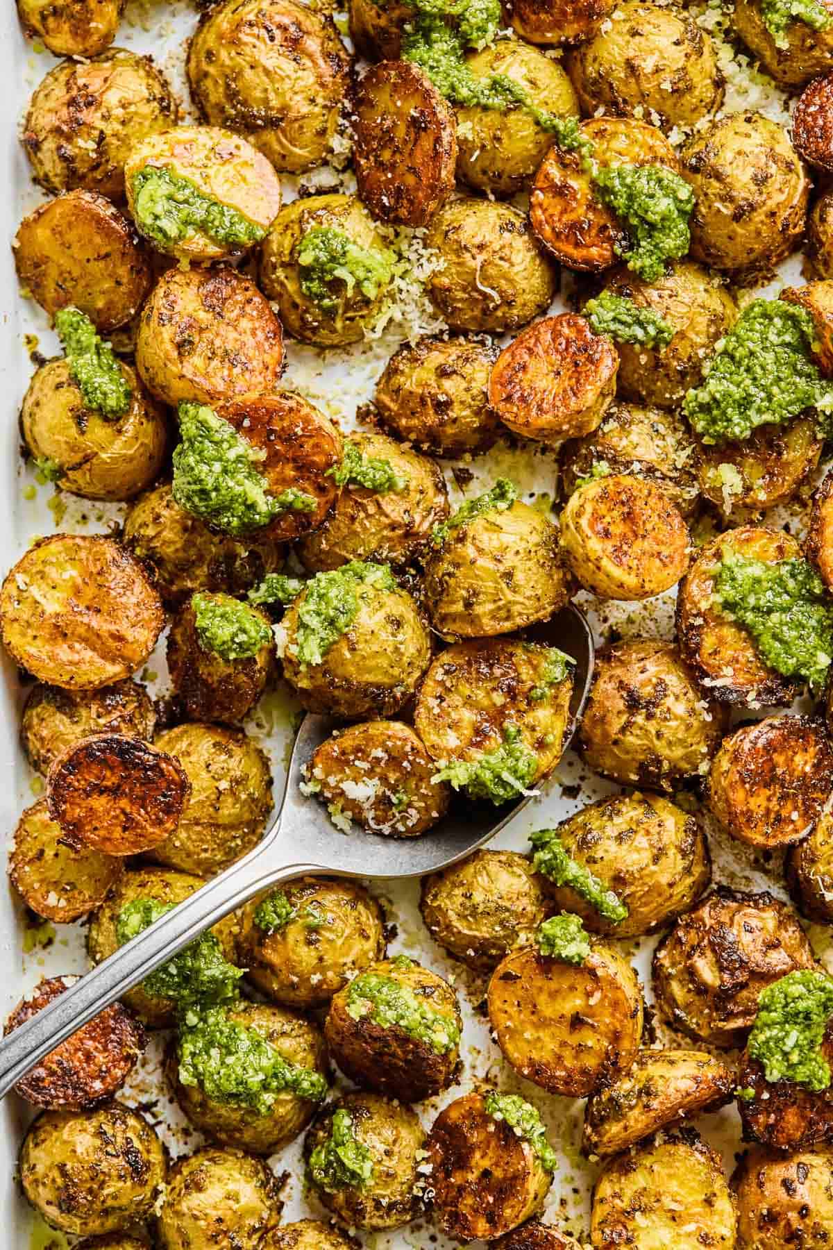 scooping up a spoonful of pesto potatoes with a serving spoon.