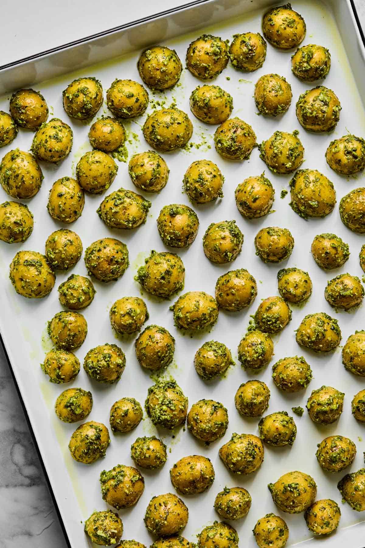 mini pesto coated potatoes arranged on a baking sheet.