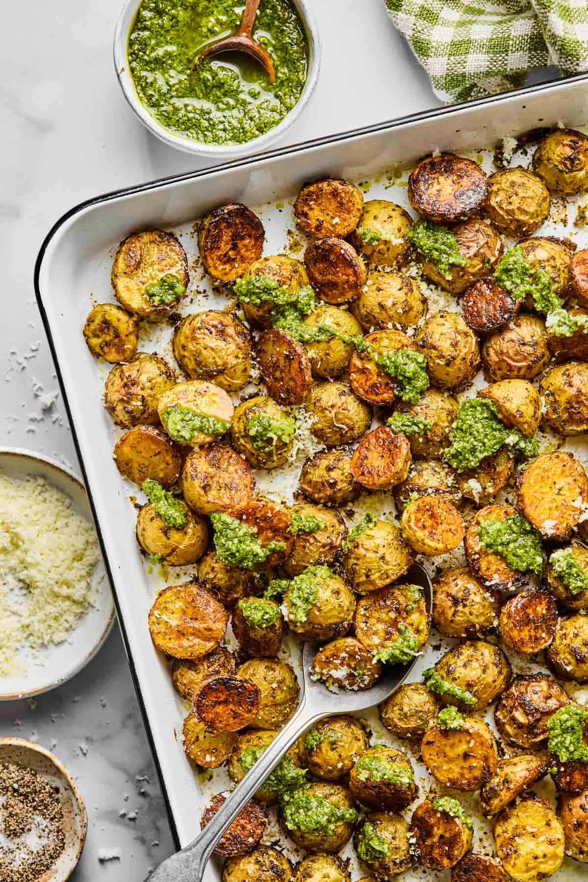 a sheet pan with crispy pesto potatoes topped with extra basil pesto.