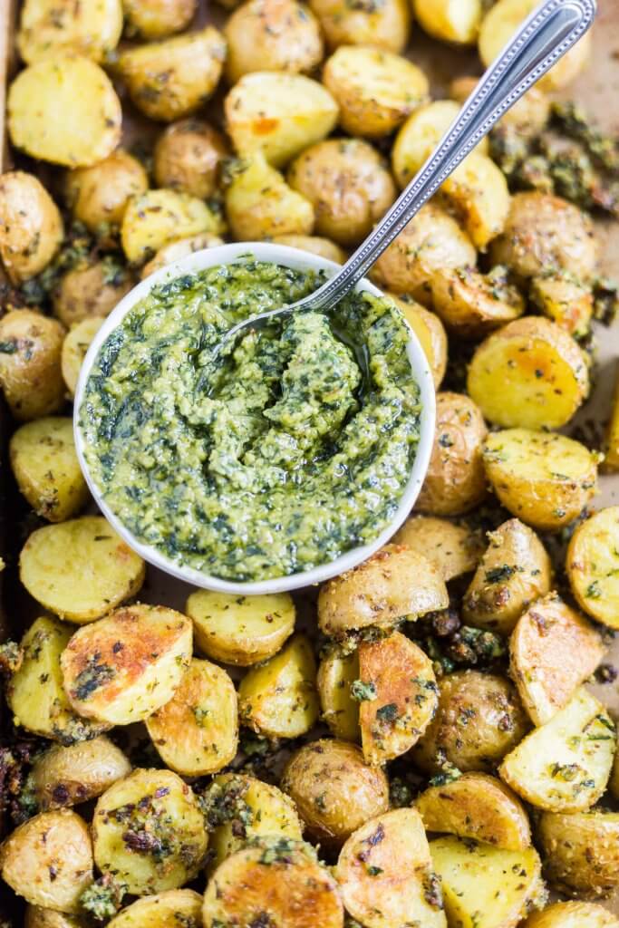 roasted pesto potatoes on a sheet pan with a bowl of fresh basil pesto with a spoon in it.