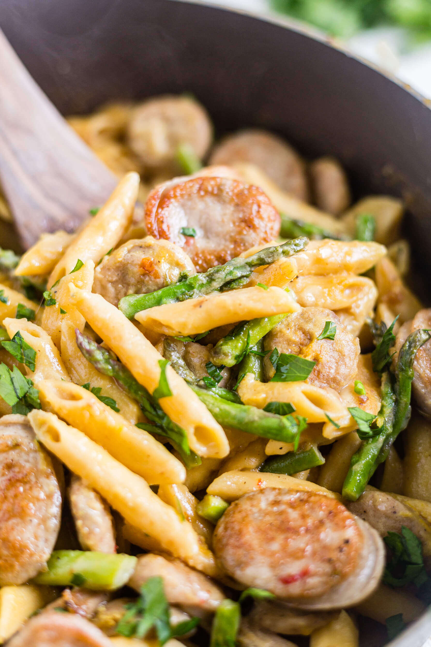 a wooden spoon scooping out chicken asparagus pasta