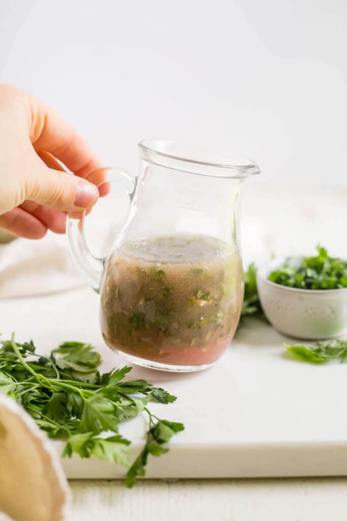 homemade fresh herb vinaigrette in a glass jar with herbs around it