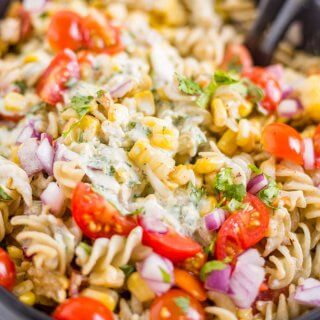 creamy jalapeno dressing on top of mexican street corn pasta salad in a black bowl with serving spoons