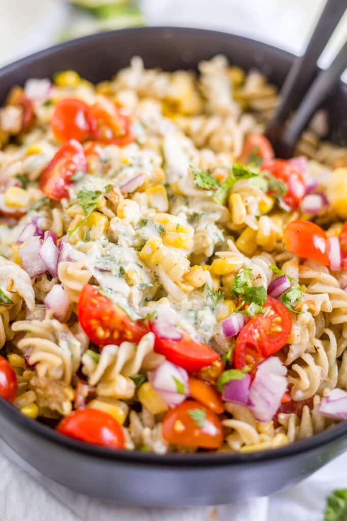 creamy jalapeno dressing on top of mexican street corn pasta salad in a black bowl with serving spoons