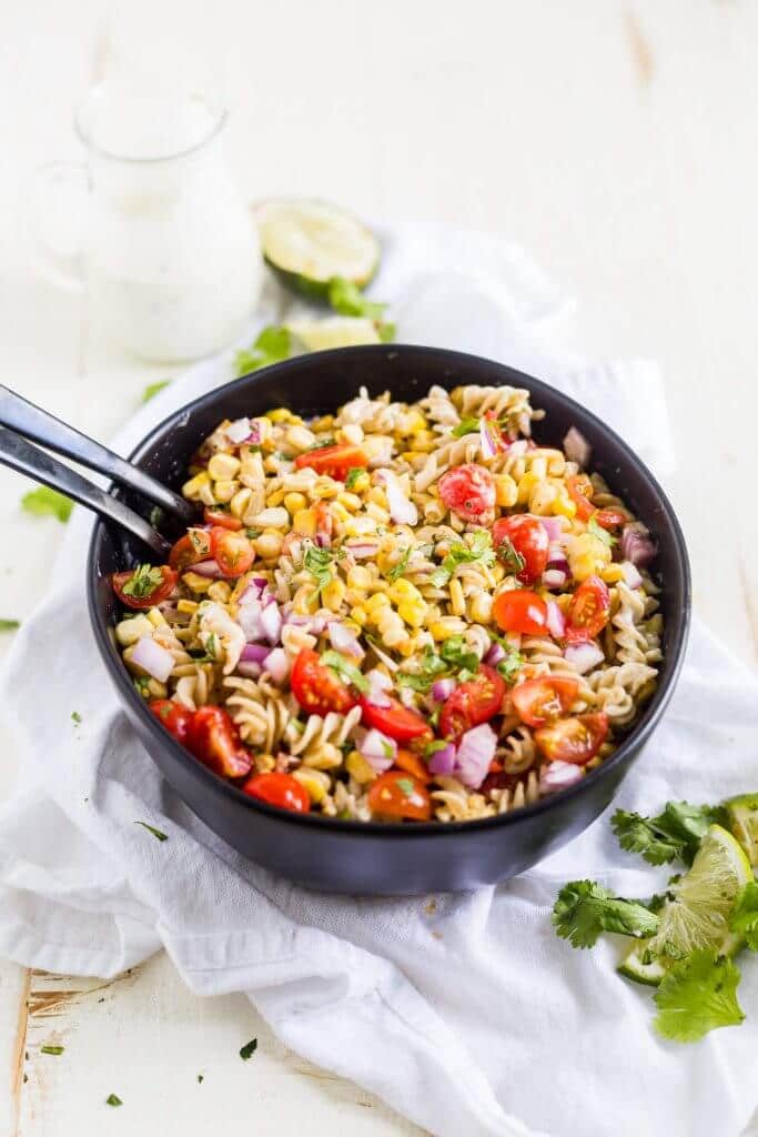 Mexican pasta salad in a black bowl with serving spoons