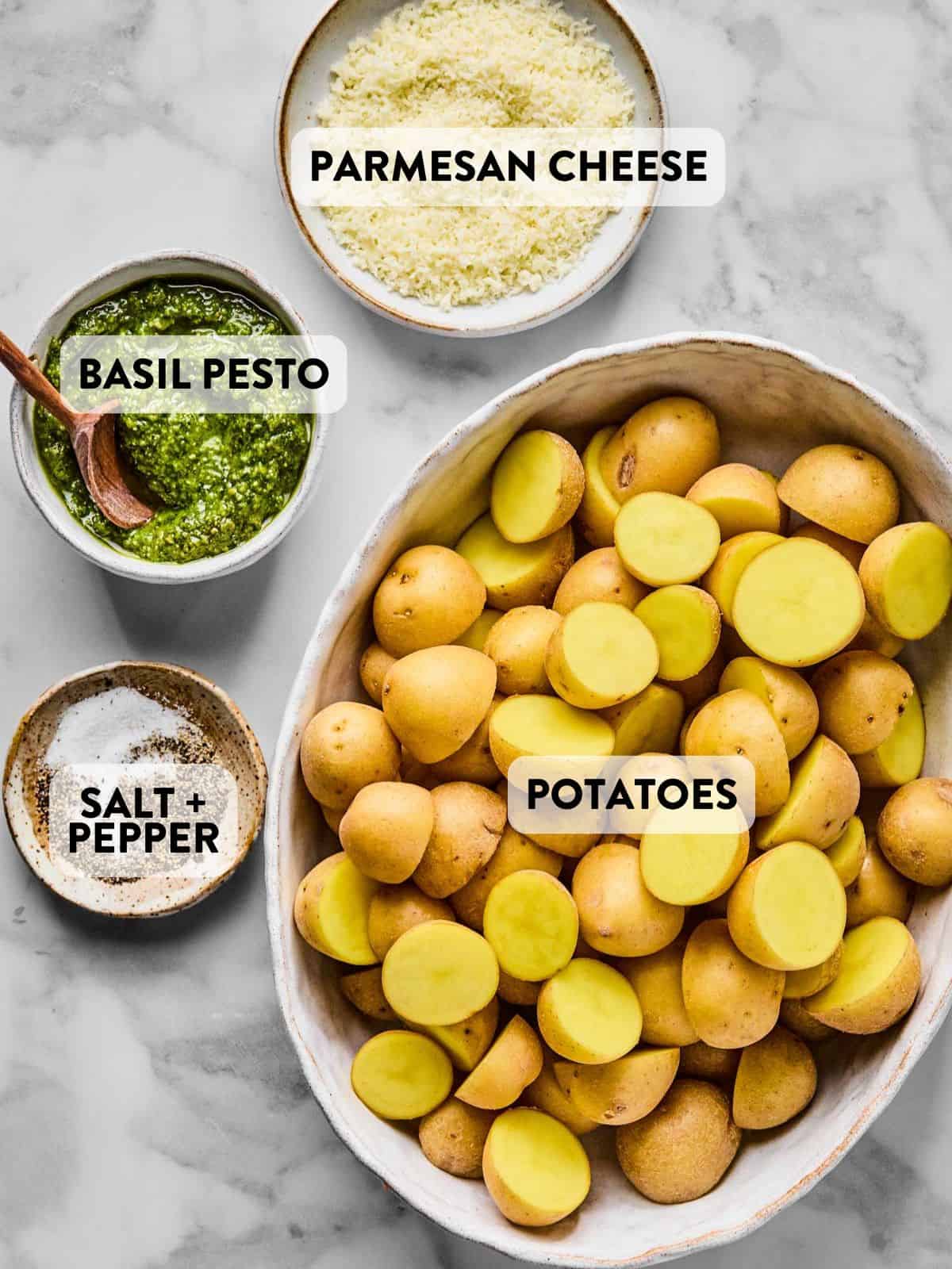 halved potatoes, parmesan cheese, and basil pesto on a counter.