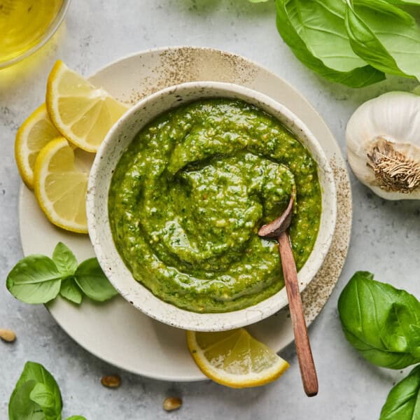 a bowl of vegan pesto with a wooden spoon and lemon and fresh basil around it.