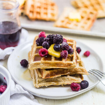 3 gluten free waffles on a white plate with butter, berries and syrup