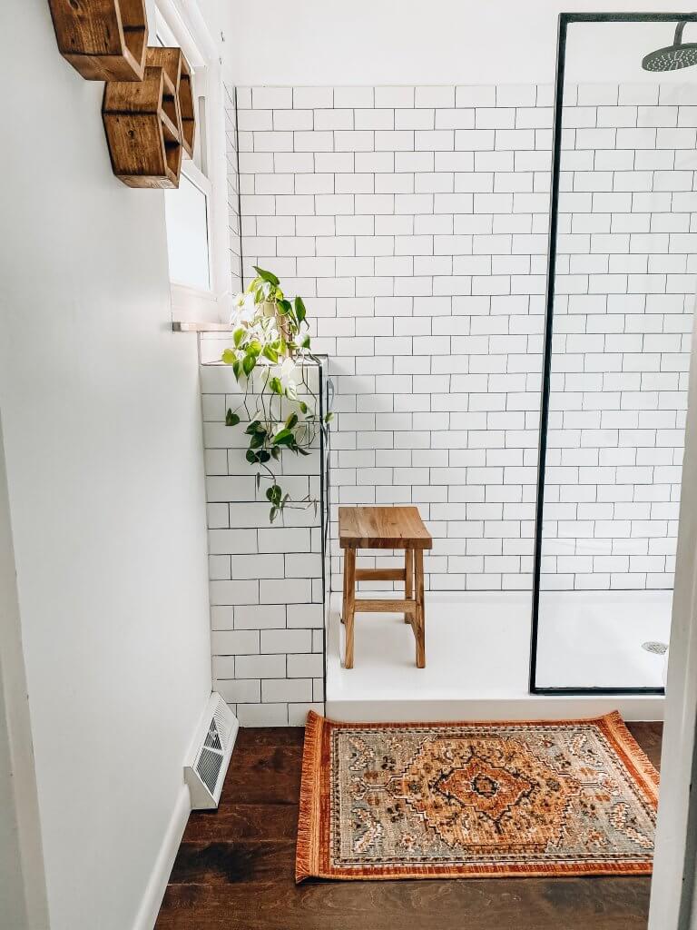 white subway tile shower with wood stool a plant and persian rug