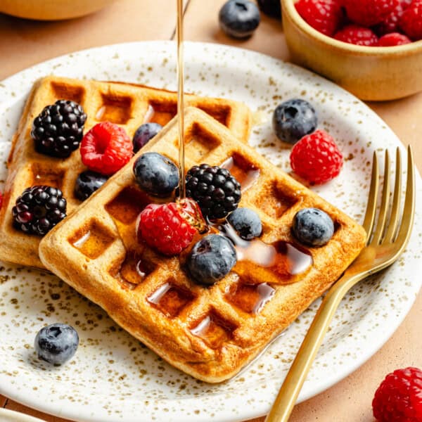 two oatmeal wafles on a speckled plate with berries and a drizzle of syrup.
