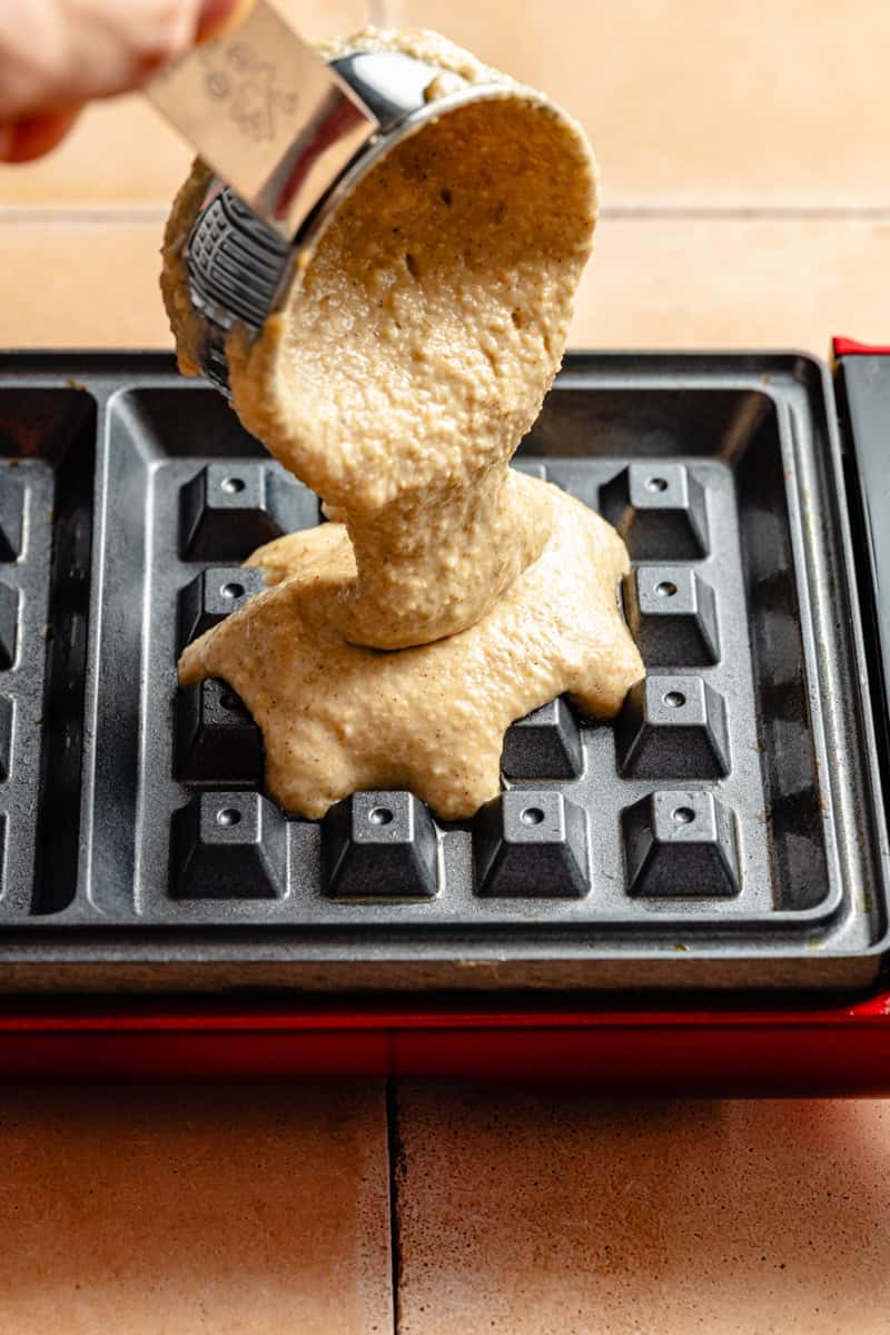 pouring oatmeal waffle batter into a hot waffle iron.