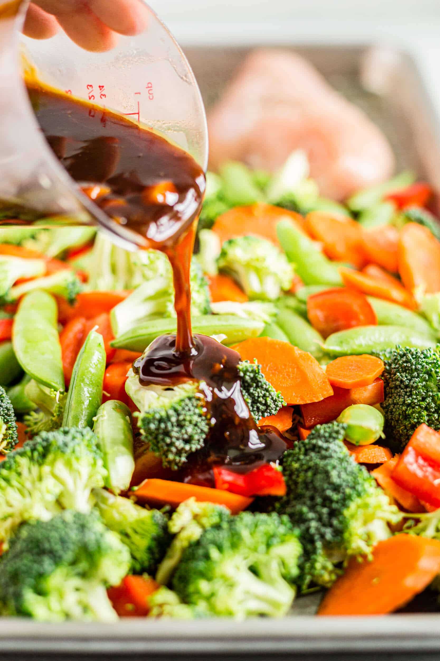 healthy teriyaki sauce being spooned over broccoli, carrots peppers and peas