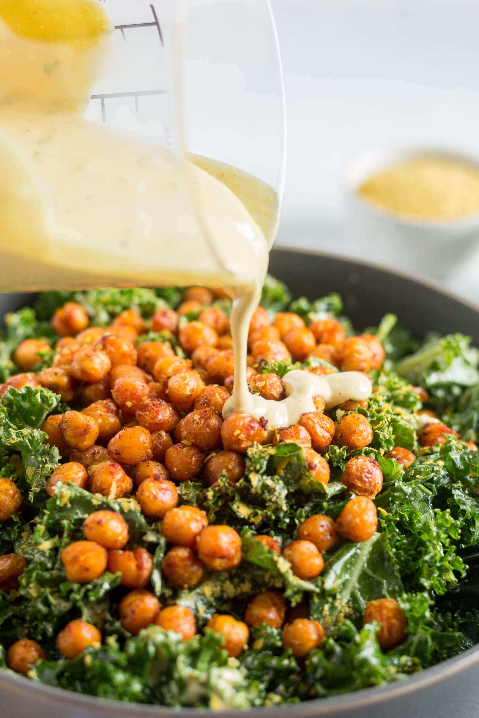 kale salt with roasted chickpeas in a grey bowl with vegan caesar dressing being poured on top