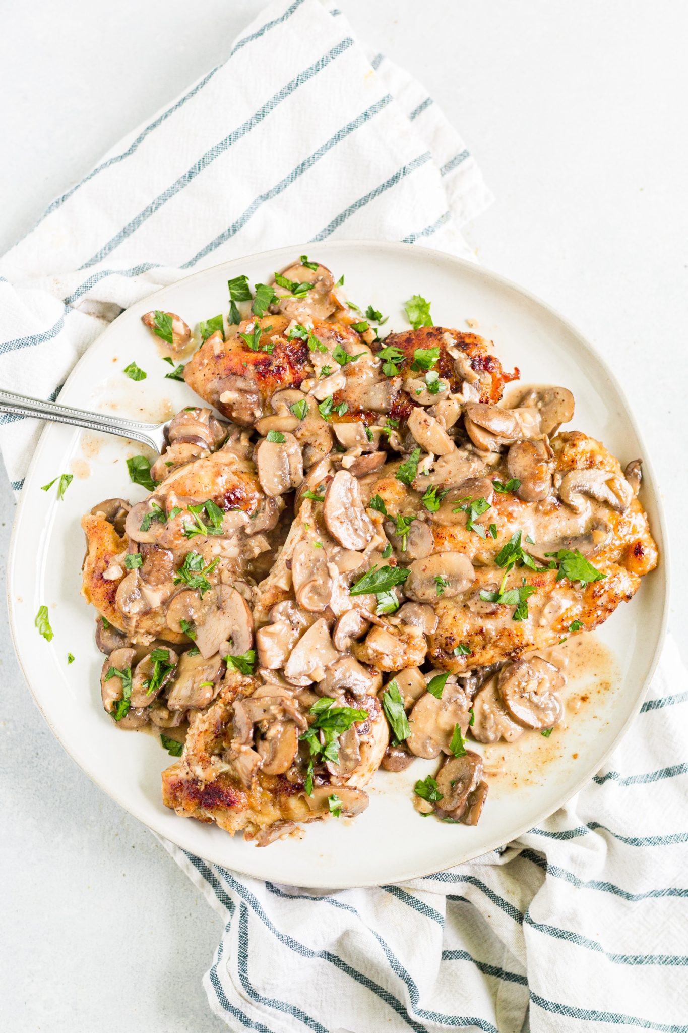 healthy chicken marsala with mushroom sauce on a white plate topped with parsley