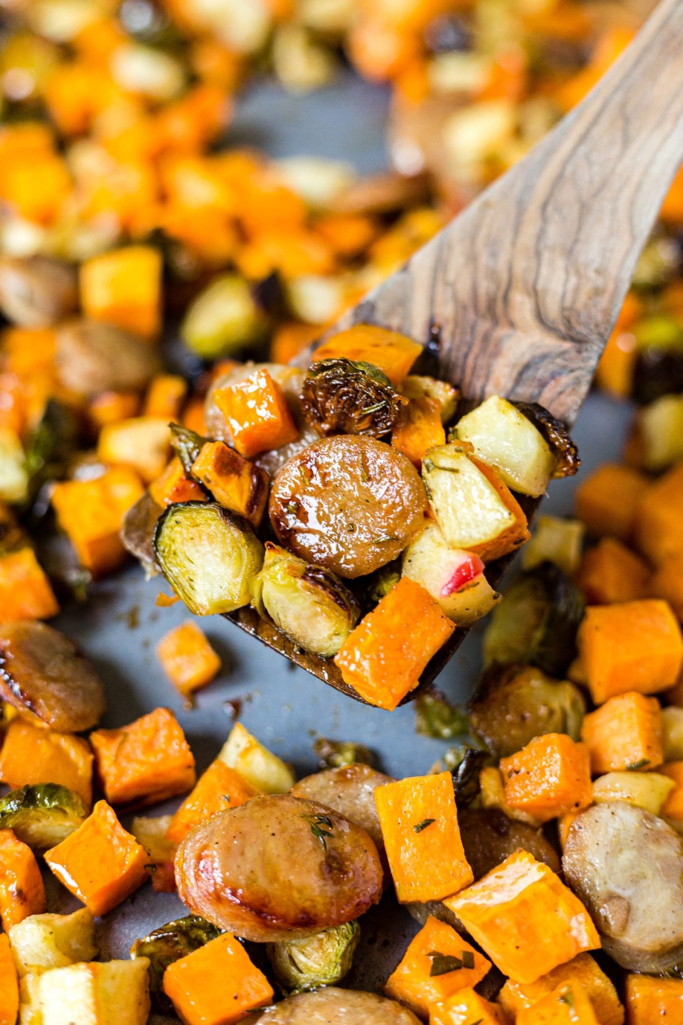 wood spatula scooping out roasted sausage and veggies off of a sheet pan