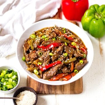 crockpot pepper steak in a white bowl with sesame seeds and green onion