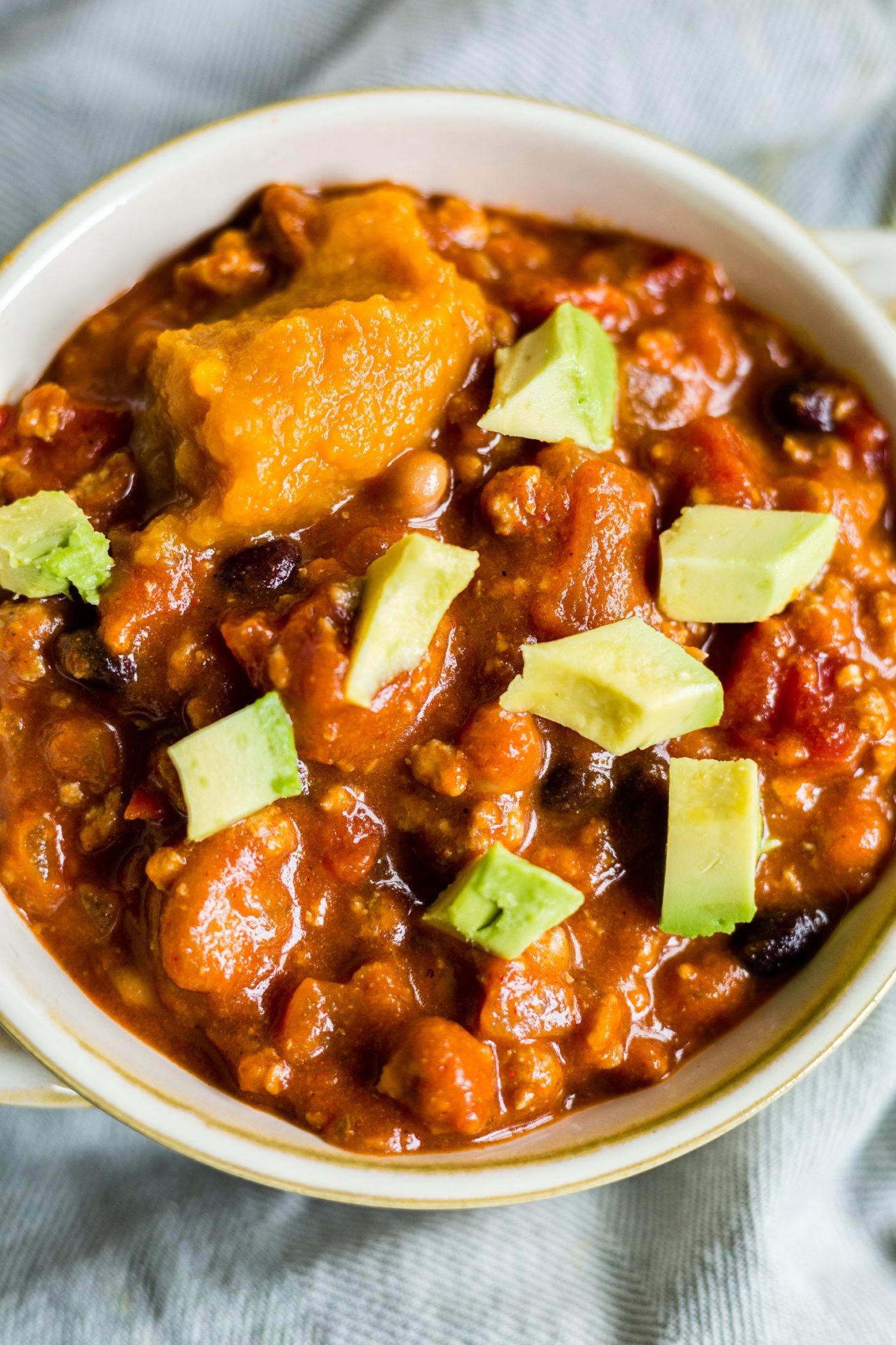 pumpkin chili in a bowl with extra pumpkin and avocado