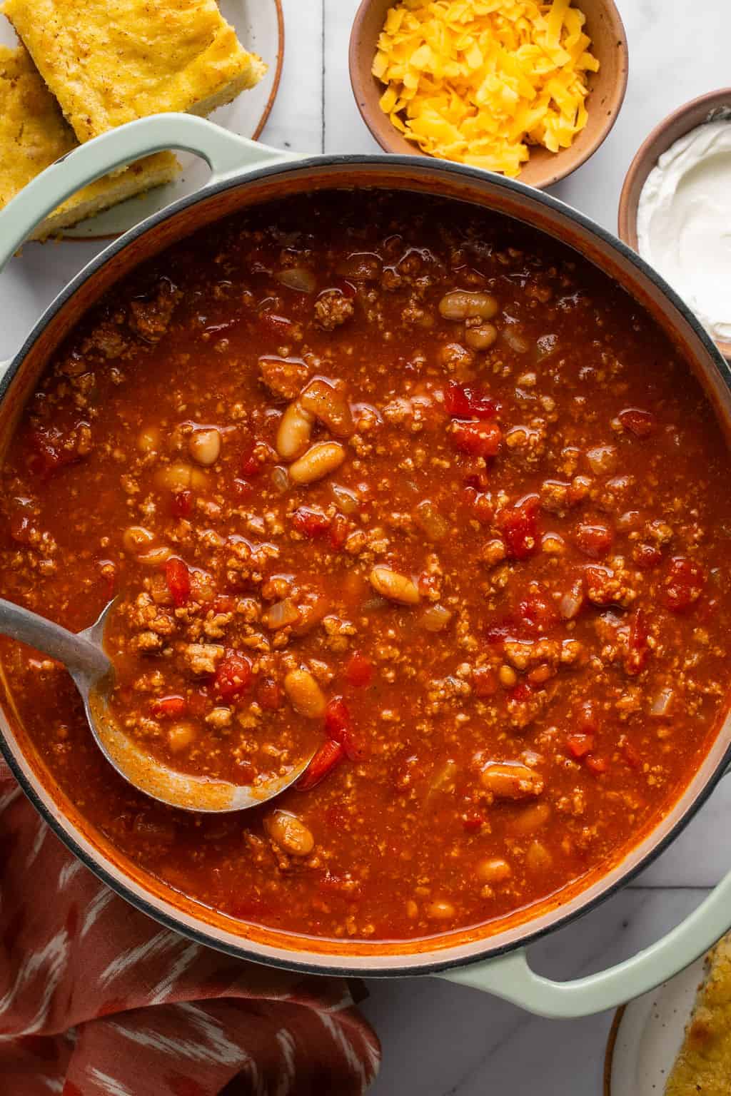 a ladle in a pot of turkey pumpkin chili with cornbread on the side.