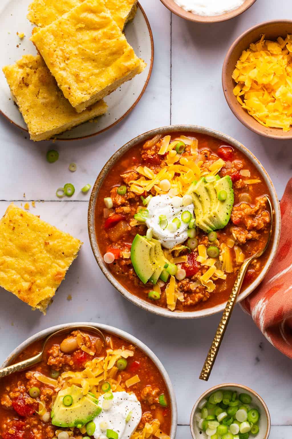 two bowls of turkey pumpkin chili with a plate of cornbread next to it.