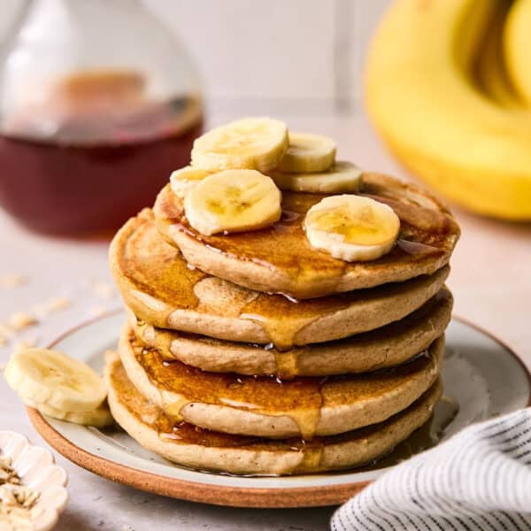 a stack of banana oat pancakes with banana slices and syrup.