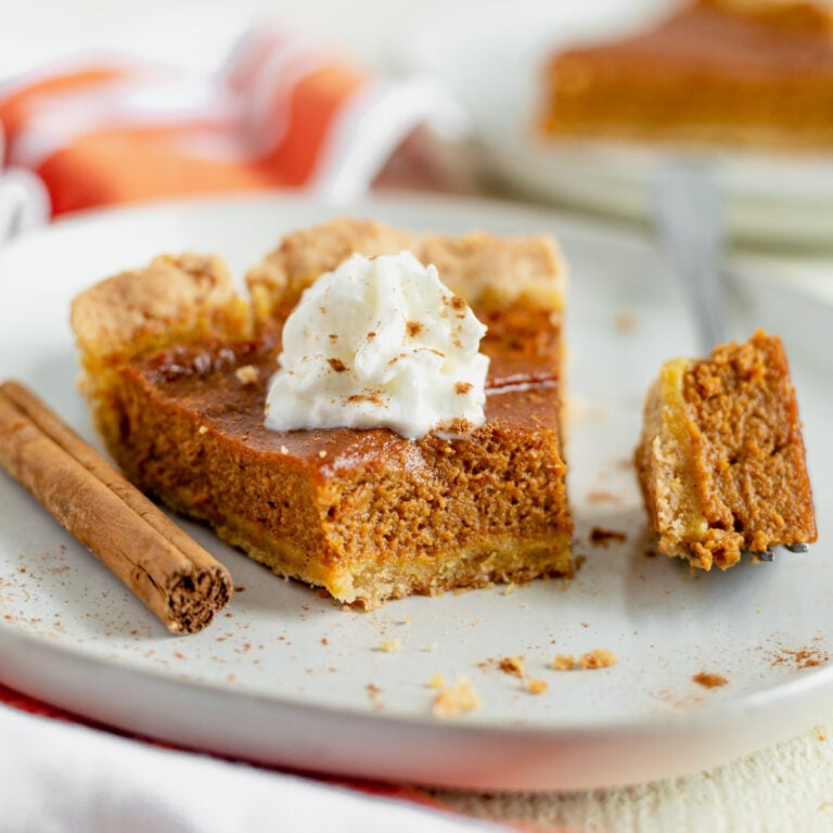 a slice of dairy free pumpkin pie on a plate topped with coconut whipped cream and a bite taken out