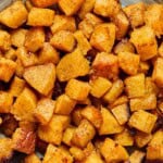 close up of roasted butternut squash pieces in a bowl with caramelized golden brown edges.