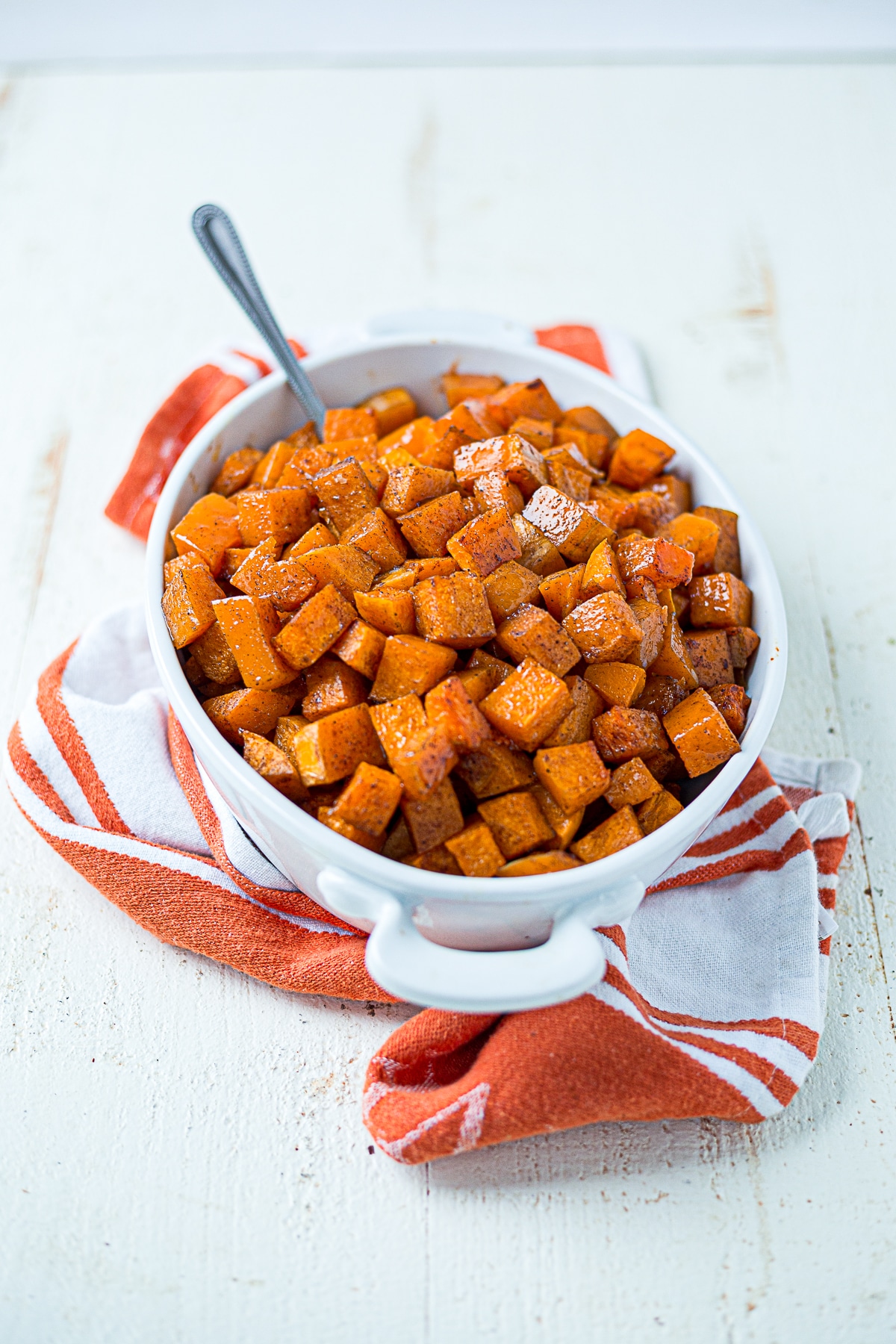 roasted butternut squash in a white bowl on an orange towel with a spoon