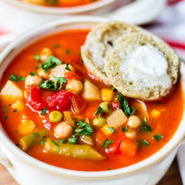 vegetable soup in a white bowl with a buttered roll on the side
