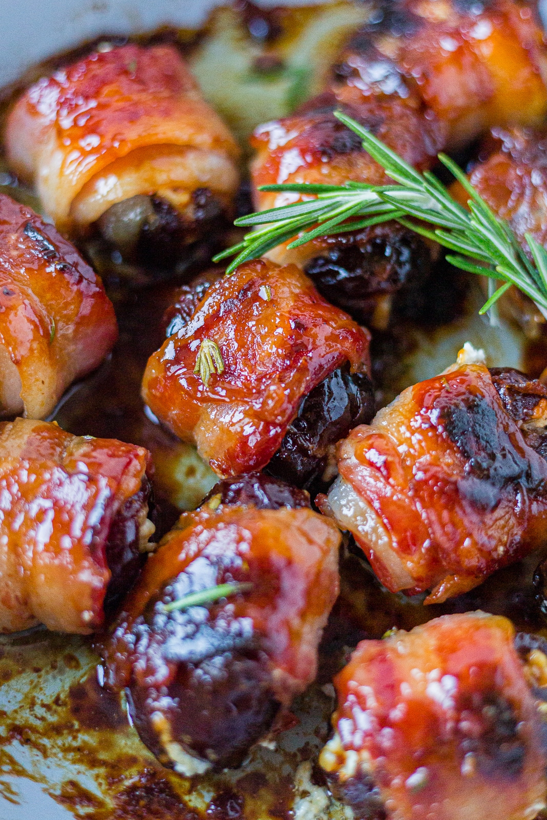 bacon wrapped dates cooked crispy on a pan with a sprig of fresh rosemary