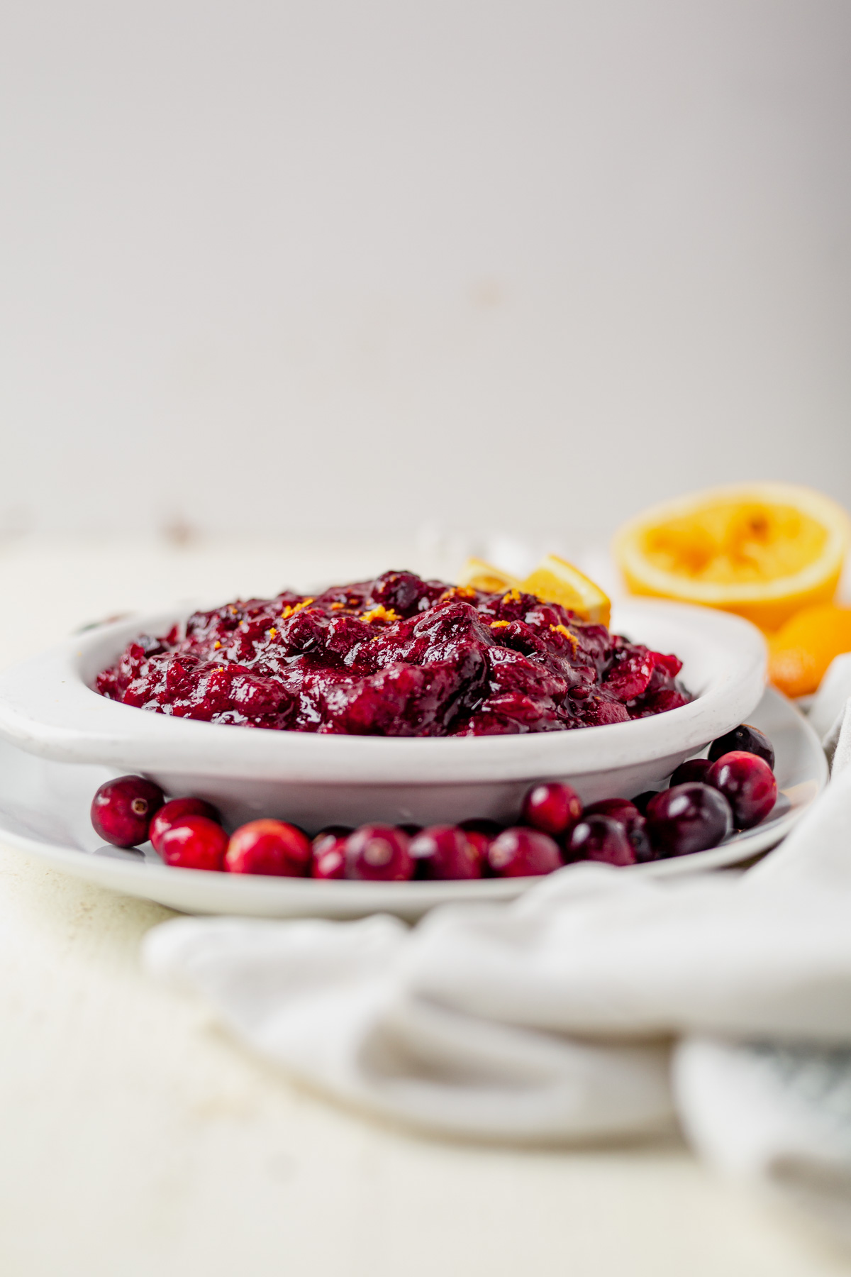 fresh cranberries and oranges surrounding a bowl of healthy cranberry sauce