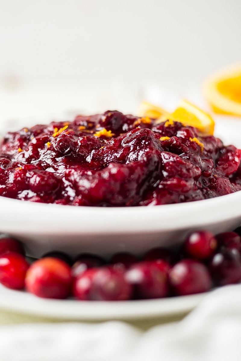 cranberry sauce in a white dish on a white plate surrounded by fresh cranberries