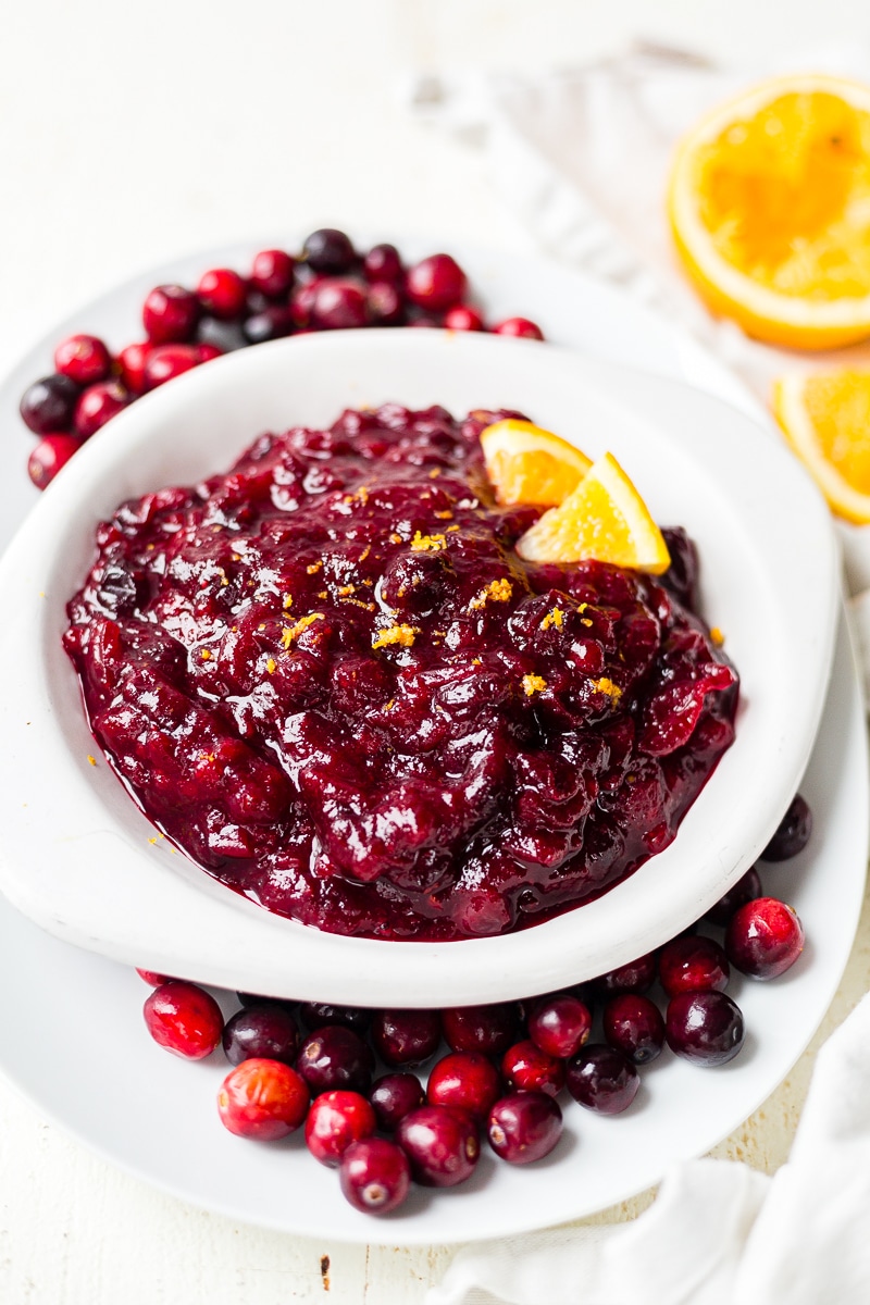 low sugar cranberry sauce sweetened with maple syrup in a serving bowl with an orange garnish