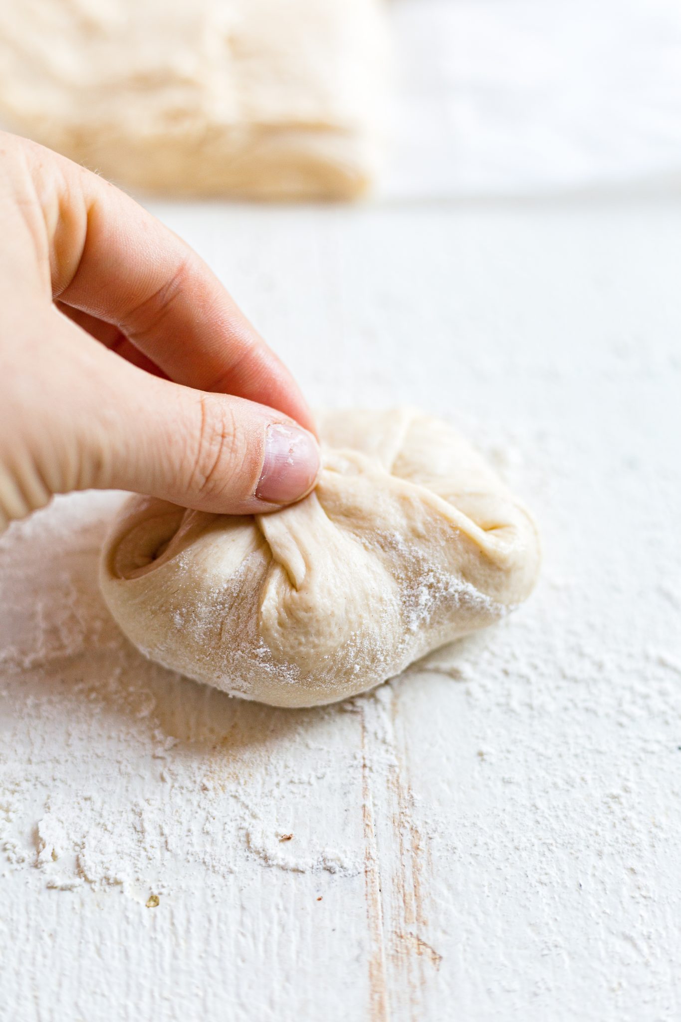 hand pinching sourdough bun dough together before rolling and baking