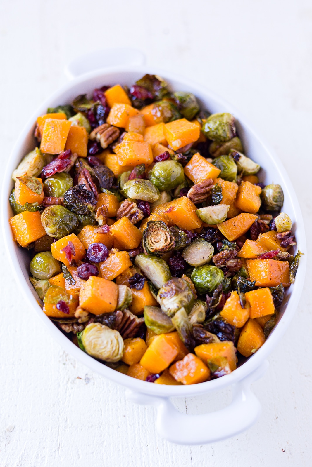 butternut squash and brussel sprouts in a serving bowl with cranberries and pecans